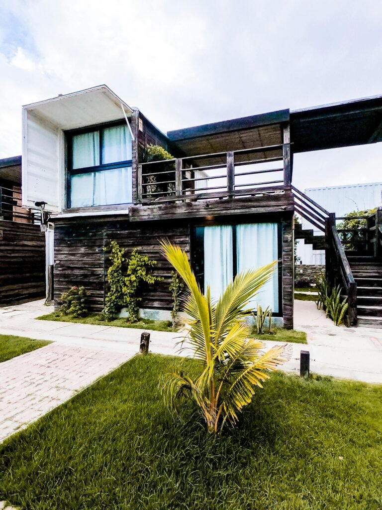 Contemporary two-story wooden house with lush greenery and palm plants.